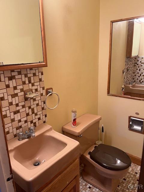 half bath featuring a sink, backsplash, and toilet