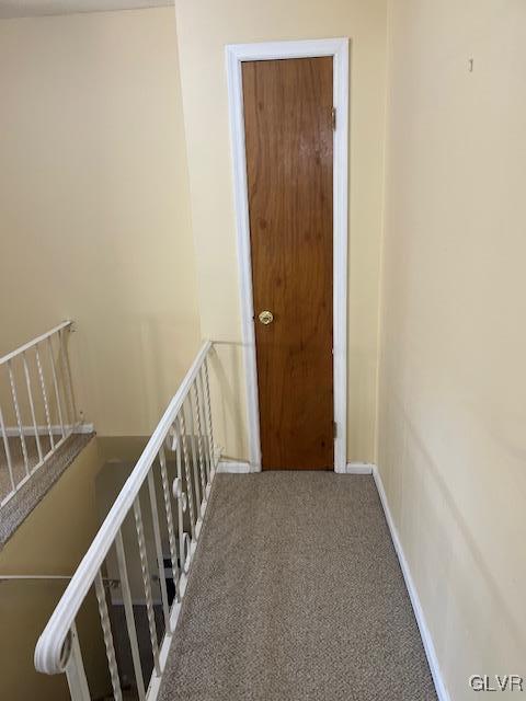 corridor with an upstairs landing, baseboards, and carpet floors