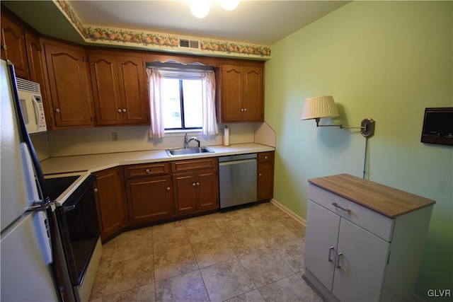 kitchen with white appliances, brown cabinetry, baseboards, visible vents, and a sink