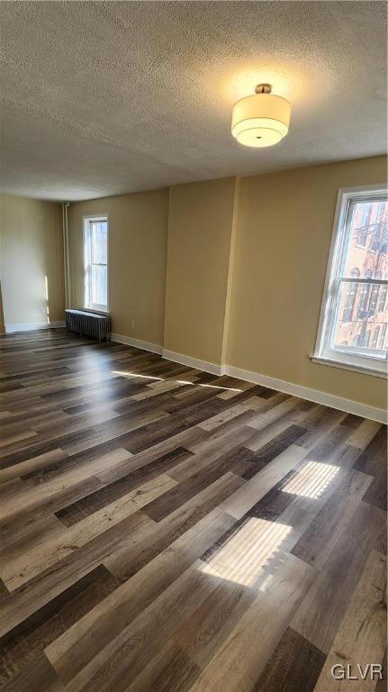 empty room with baseboards, radiator, dark wood-style floors, and a textured ceiling