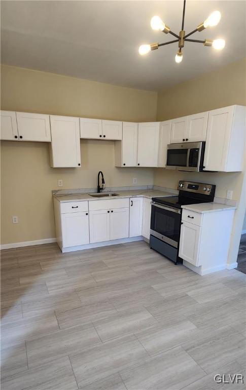 kitchen with a sink, appliances with stainless steel finishes, light countertops, and white cabinetry