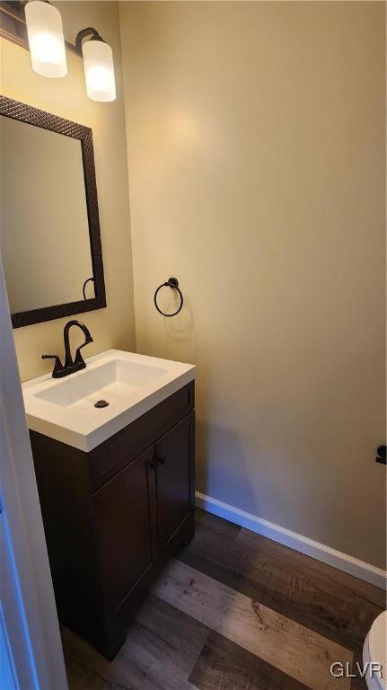 bathroom featuring baseboards, toilet, wood finished floors, and vanity