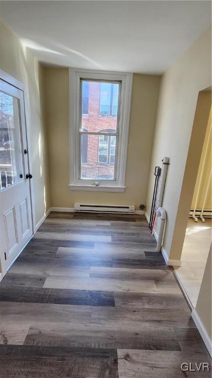 empty room featuring wood finished floors, baseboards, and a baseboard radiator