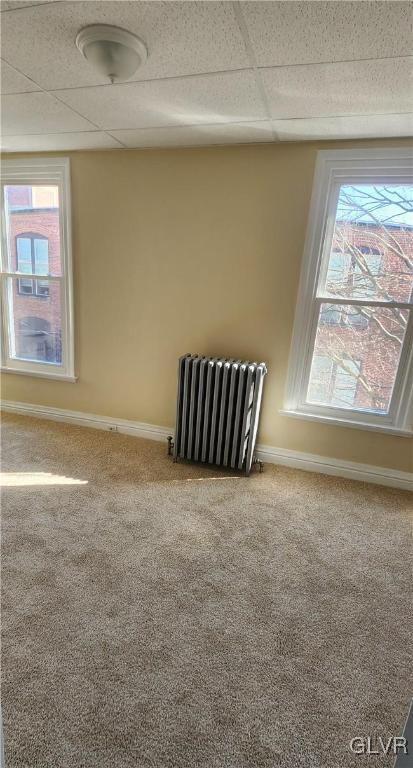 unfurnished room with baseboards, radiator, and carpet