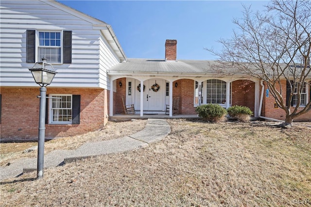 tri-level home with a porch, brick siding, and a chimney