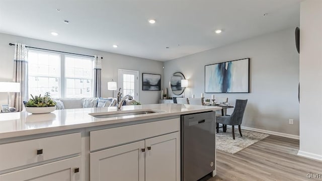 kitchen featuring light wood-type flooring, a sink, open floor plan, light countertops, and dishwasher