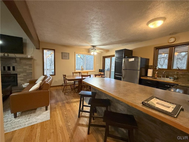 248 Penn Forest Trl, Penn Forest Township, PA 18210 - kitchen featuring light wood finished floors, a kitchen bar, a fireplace, freestanding refrigerator, and a sink