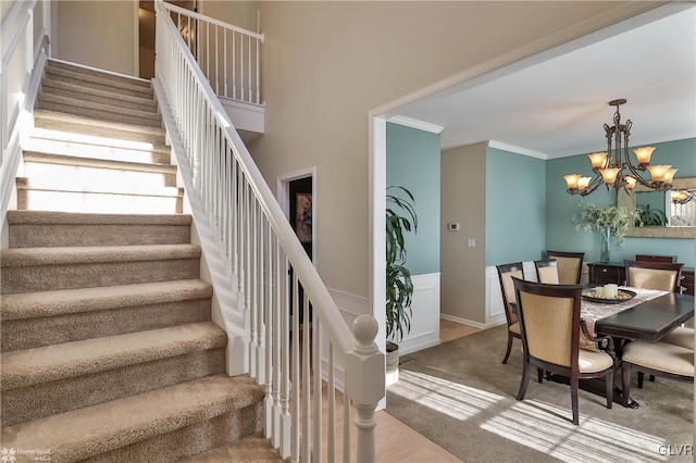 dining space with crown molding, a wainscoted wall, stairs, a notable chandelier, and a decorative wall