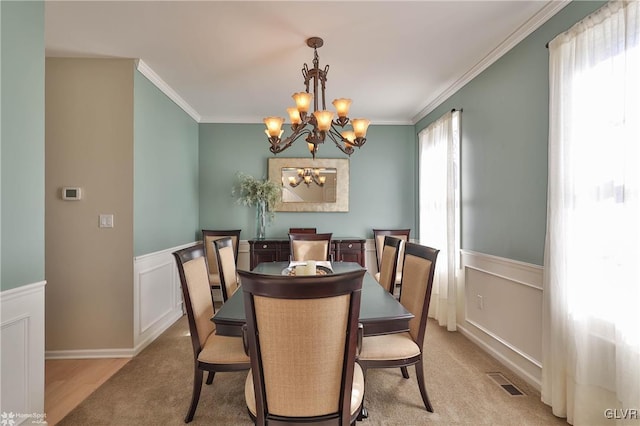 dining space with visible vents, an inviting chandelier, wainscoting, crown molding, and light colored carpet