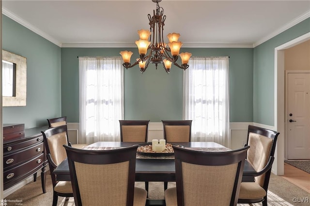 carpeted dining area with plenty of natural light, crown molding, an inviting chandelier, and a wainscoted wall