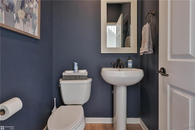 half bath with toilet, wood finished floors, baseboards, and a sink