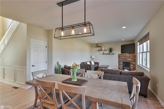 dining room featuring visible vents, light wood-style flooring, a stone fireplace, stairs, and a decorative wall