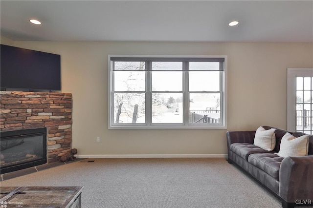 living room with a wealth of natural light, baseboards, carpet, and a stone fireplace