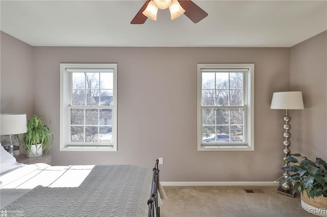 carpeted bedroom with visible vents, multiple windows, baseboards, and ceiling fan