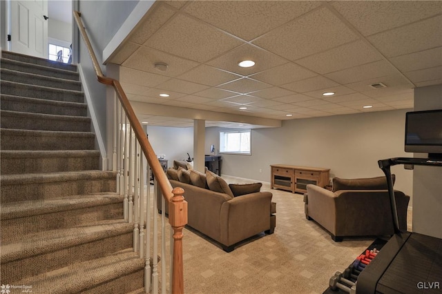 living area featuring a drop ceiling, stairway, baseboards, and light colored carpet