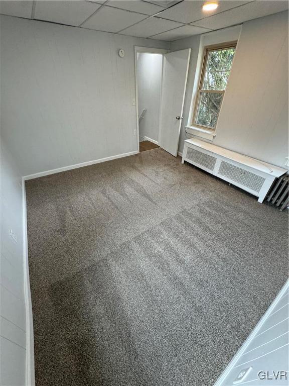 interior space featuring a drop ceiling, radiator heating unit, and baseboards