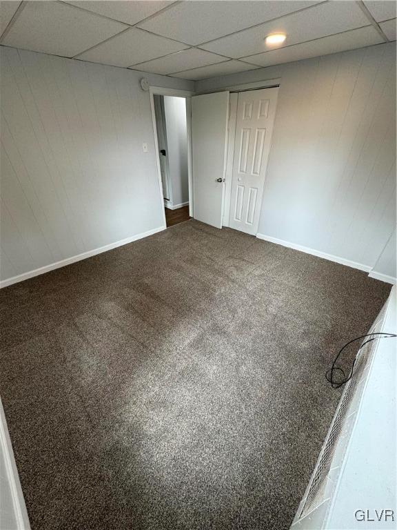 unfurnished bedroom with a closet, baseboards, dark colored carpet, and a drop ceiling