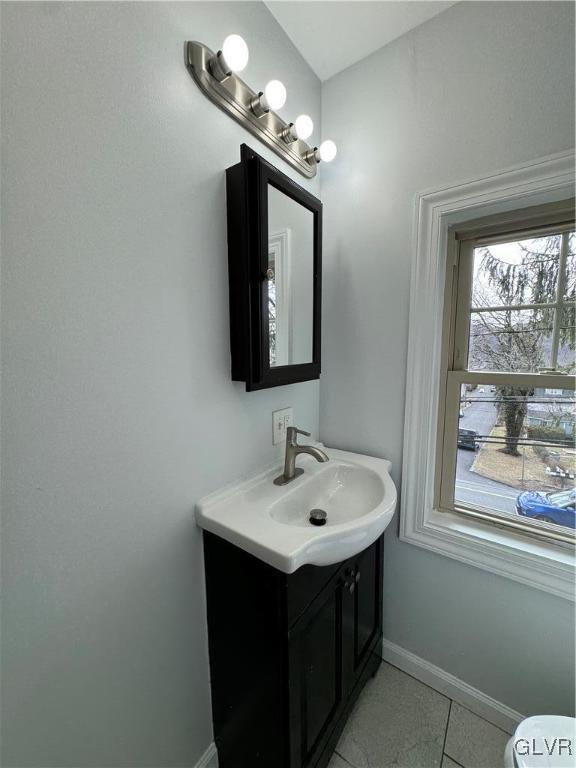 half bath with baseboards, vanity, and tile patterned flooring