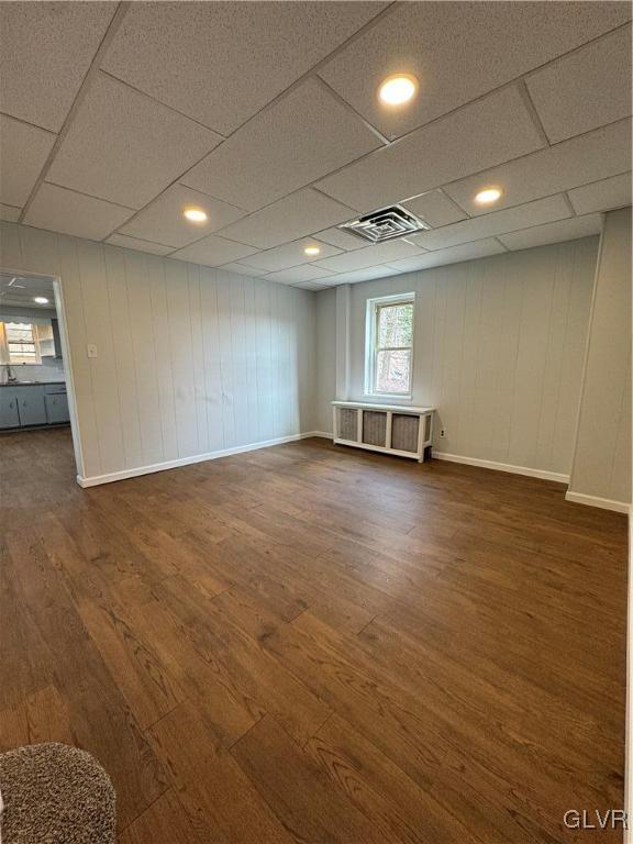 below grade area with visible vents, a paneled ceiling, baseboards, and wood finished floors