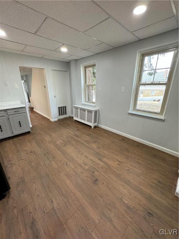 unfurnished room with visible vents, baseboards, radiator heating unit, dark wood-type flooring, and a paneled ceiling