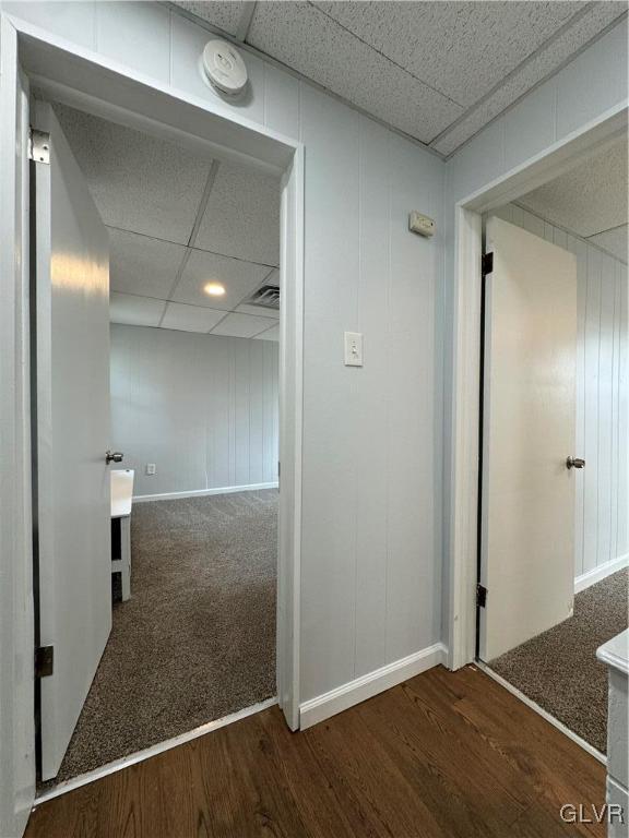 corridor featuring visible vents, a paneled ceiling, baseboards, and wood finished floors