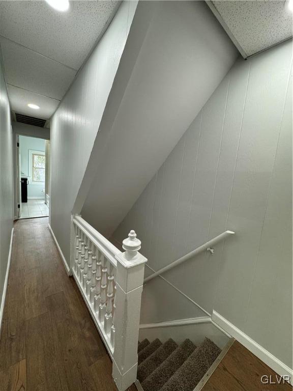 staircase with a drop ceiling, baseboards, visible vents, and wood finished floors