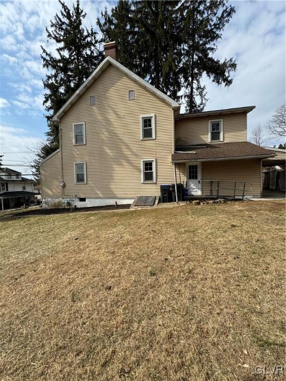 rear view of property with a carport, a yard, central AC, and a chimney