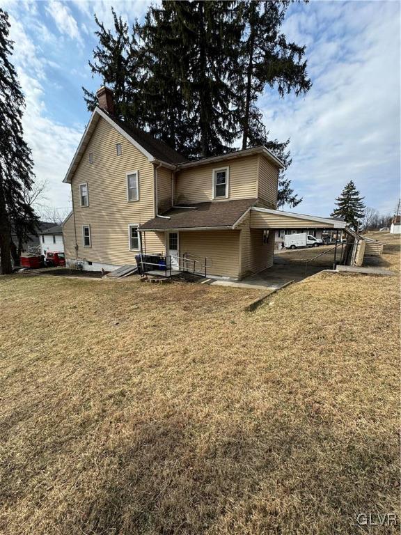 rear view of property with a chimney, an attached carport, and a lawn