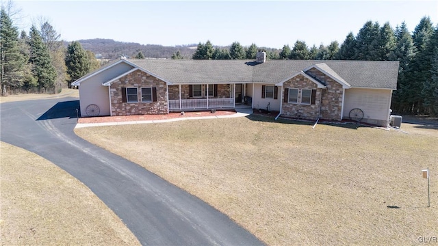 ranch-style home with stone siding, covered porch, a chimney, and roof with shingles