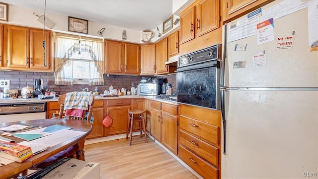 kitchen featuring under cabinet range hood, light countertops, decorative backsplash, light wood-style flooring, and stainless steel appliances