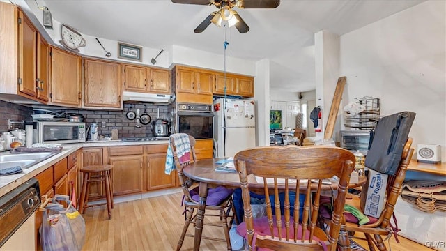 kitchen with black oven, under cabinet range hood, light countertops, dishwashing machine, and freestanding refrigerator