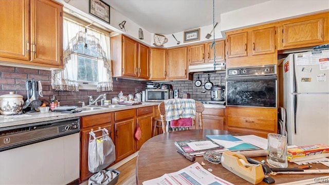 kitchen featuring under cabinet range hood, light countertops, decorative backsplash, white appliances, and a sink