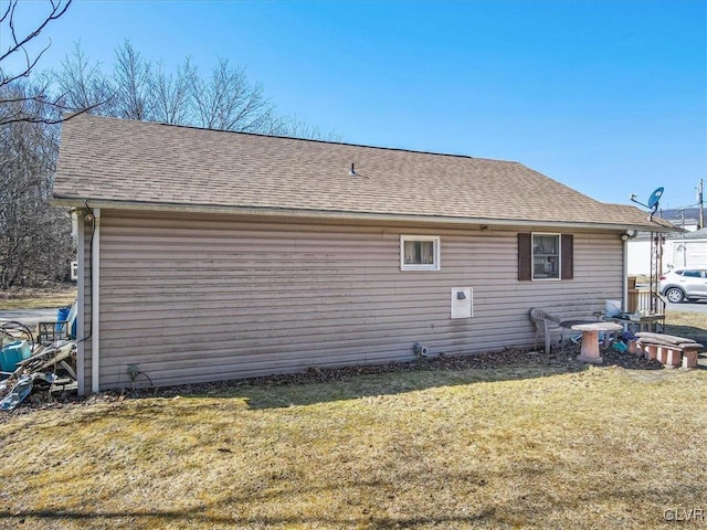 rear view of house featuring a yard and roof with shingles