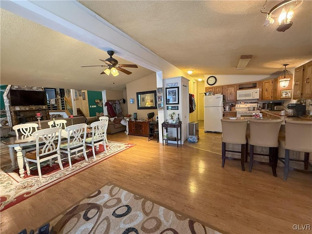 dining room with light wood finished floors, a textured ceiling, ceiling fan, and vaulted ceiling