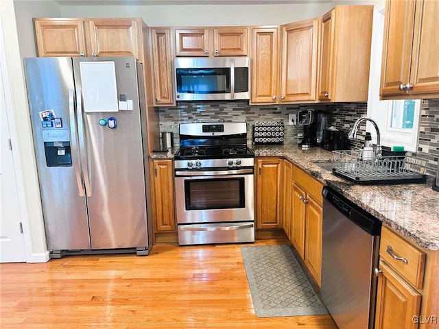 kitchen featuring a sink, tasteful backsplash, appliances with stainless steel finishes, light wood finished floors, and stone counters