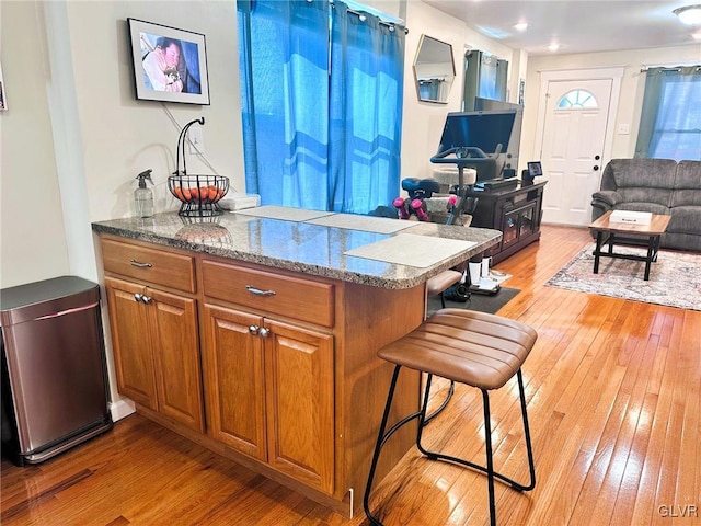 kitchen with brown cabinets, a breakfast bar, stone countertops, light wood-style floors, and open floor plan