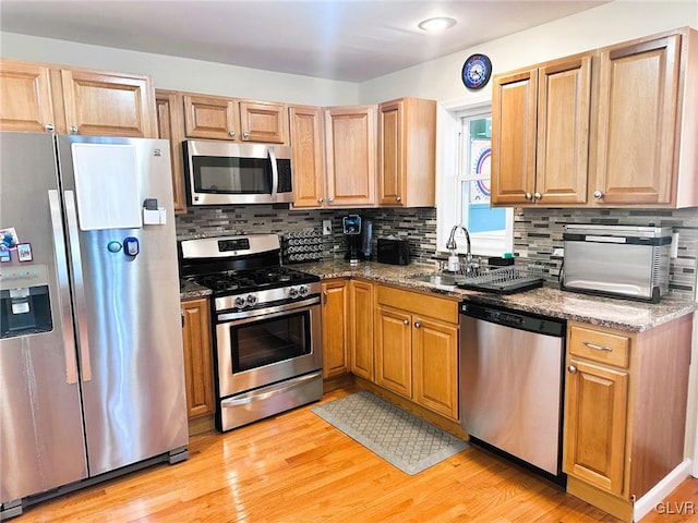 kitchen featuring light wood-style flooring, a sink, stone countertops, appliances with stainless steel finishes, and decorative backsplash