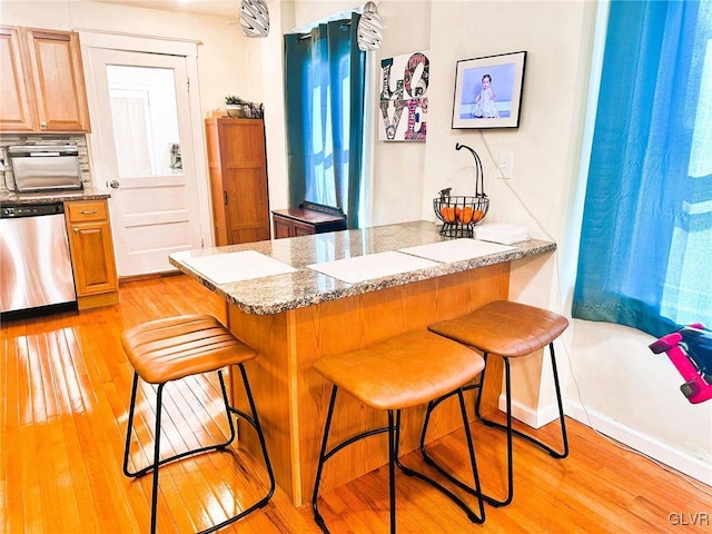 kitchen with light wood-style flooring, dishwasher, a breakfast bar area, and a peninsula