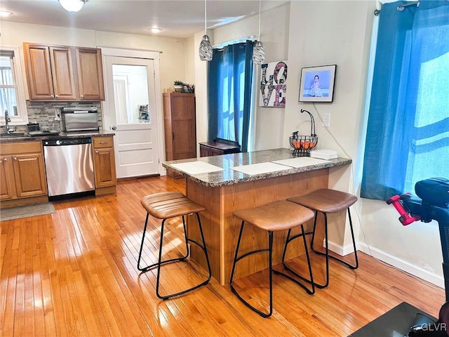 kitchen featuring a breakfast bar area, a peninsula, light wood-style flooring, stainless steel dishwasher, and backsplash