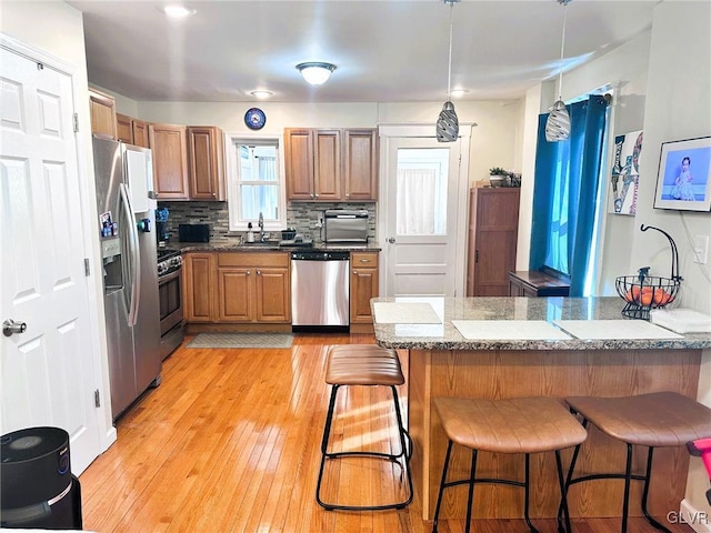 kitchen featuring a sink, a kitchen breakfast bar, brown cabinetry, and stainless steel appliances