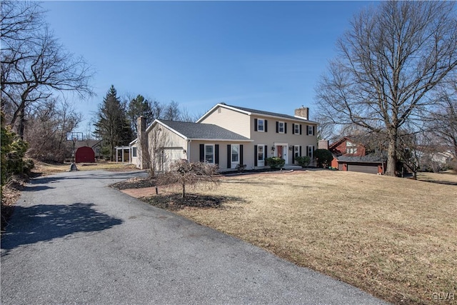 colonial home featuring a garage, driveway, a front lawn, and a chimney