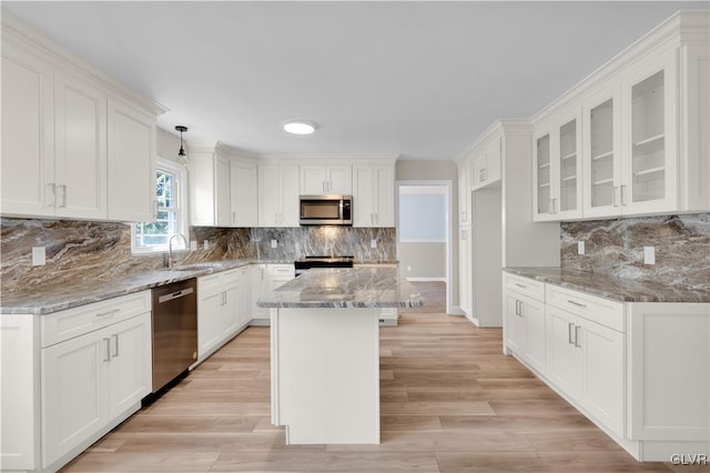 kitchen featuring glass insert cabinets, light wood-type flooring, light stone counters, stainless steel appliances, and white cabinetry