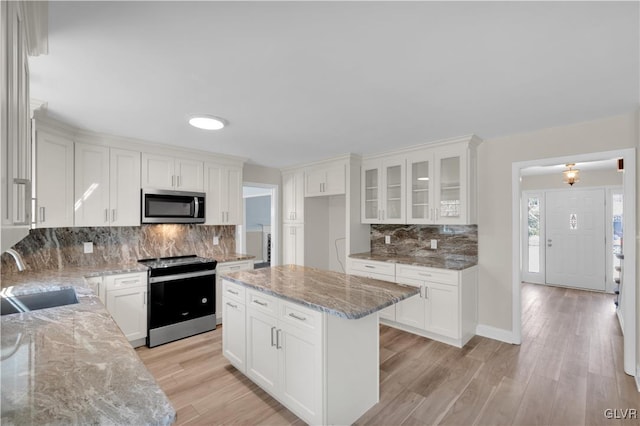 kitchen with glass insert cabinets, light stone countertops, light wood-style floors, stainless steel appliances, and a sink