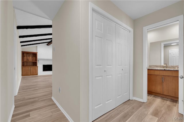 hallway featuring lofted ceiling with beams, light wood-style flooring, baseboards, and a sink