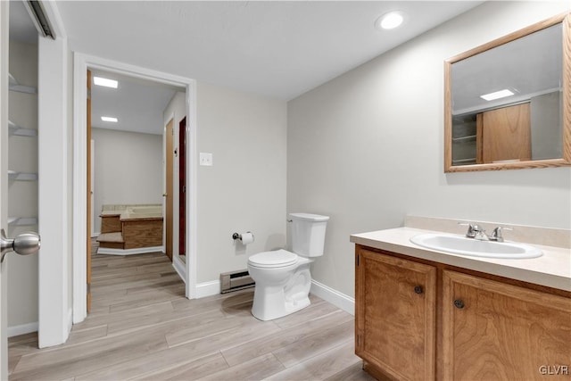 bathroom with baseboards, toilet, baseboard heating, wood finished floors, and vanity