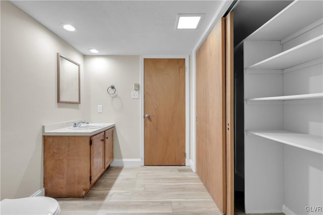 bathroom featuring toilet, wood finished floors, recessed lighting, baseboards, and vanity