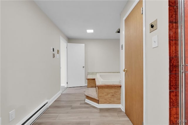 corridor with a baseboard heating unit, light wood-style floors, and baseboards