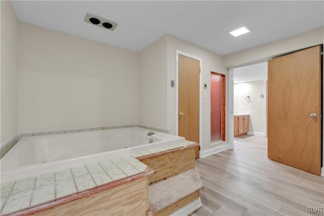 bathroom with a bath, wood finished floors, and baseboards