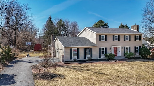 colonial house featuring a front lawn, an attached garage, driveway, and a chimney