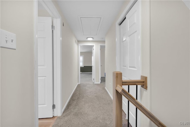 hallway with an upstairs landing, light carpet, attic access, and baseboards